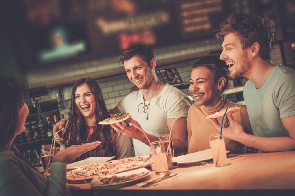 Cheerful multiracial friends having fun eating in pizzeria.